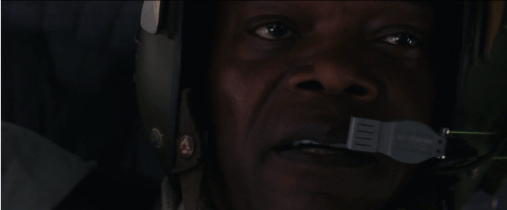 Imagem em close de Samuel L. Jackson, interpretando o tenente Preston Packard na cena em que conta o mito sobre as asas de ícaro. Ele usa capacete e comunicador, pois está na cabine de um helicóptero de combate.